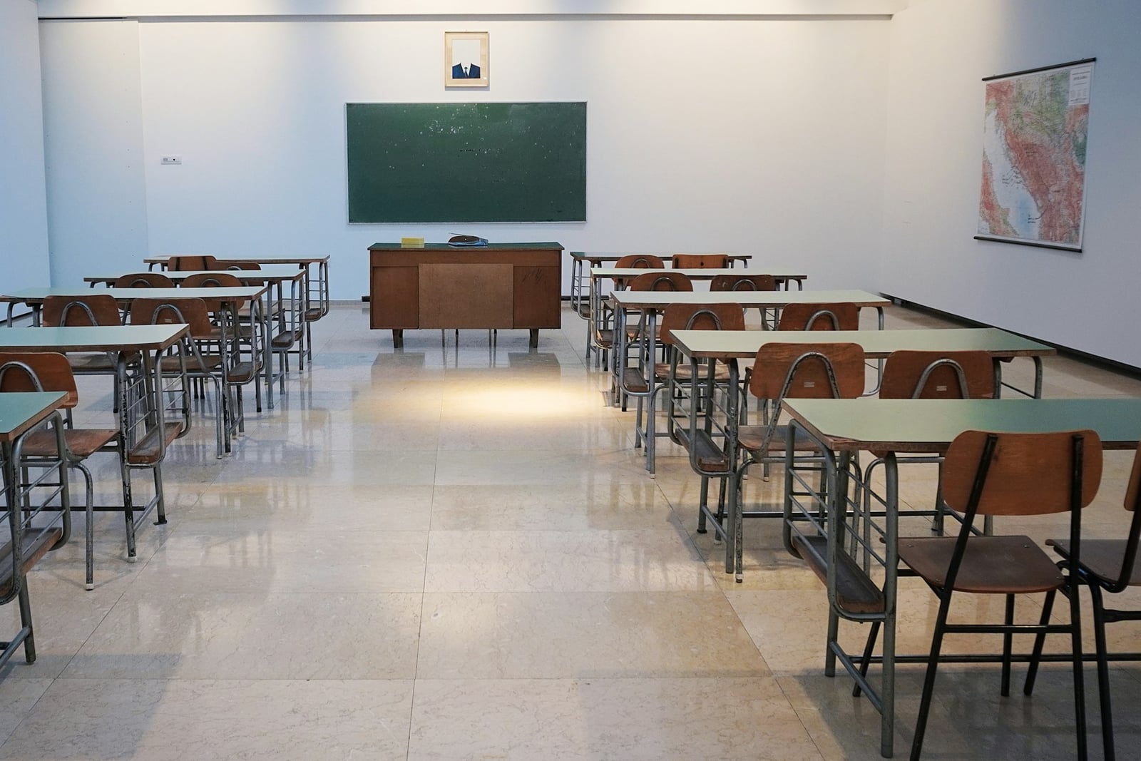 An empty white classroom with mint-green desks and a chalkboard