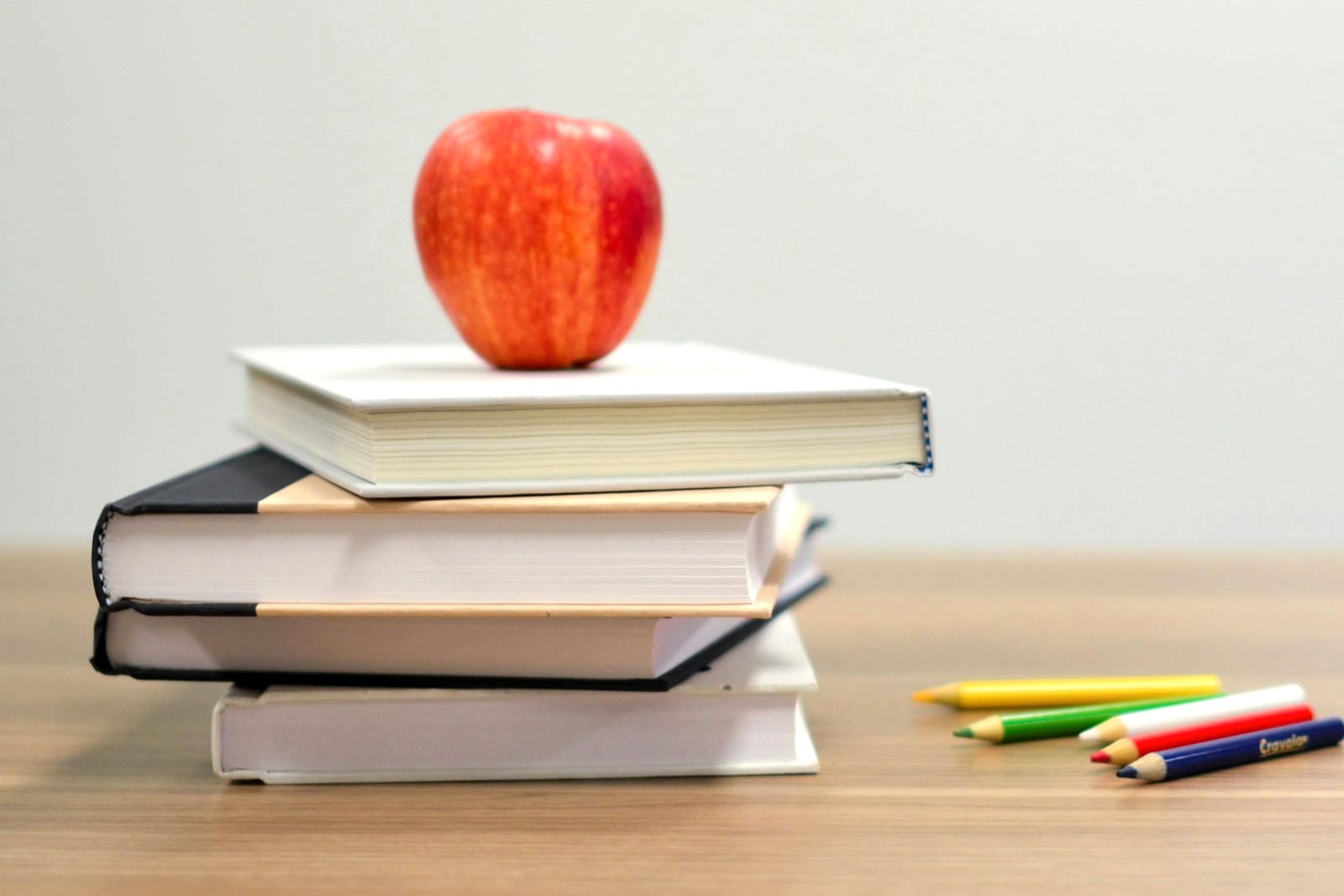 A red apple resting on a stack of books beside coloured pencils